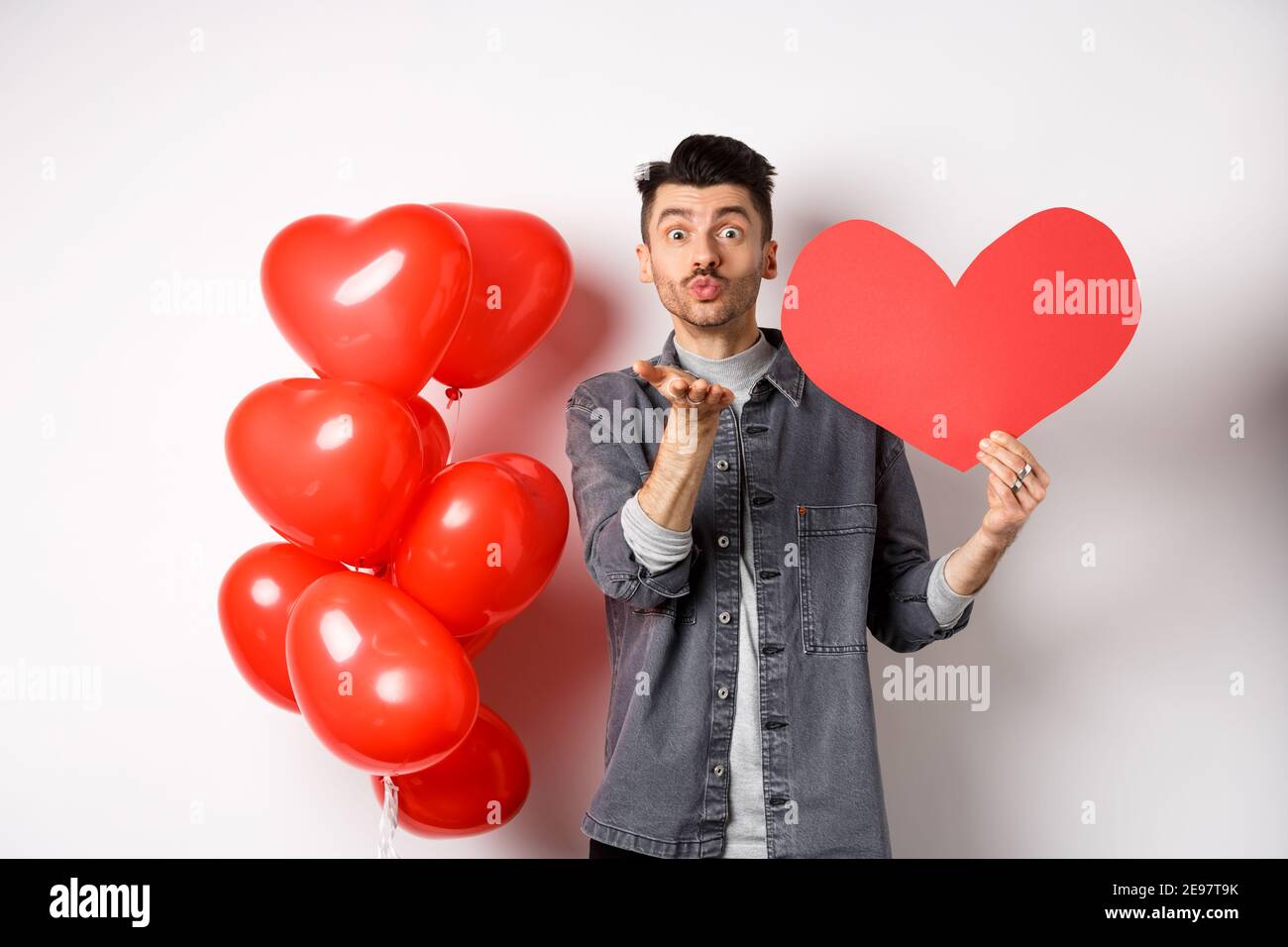 El concepto del día de San Valentín. Hombre soñando con el amor verdadero,  sosteniendo un corte de corazón rojo y parado cerca de globos románticos,  fondo azul Fotografía de stock - Alamy
