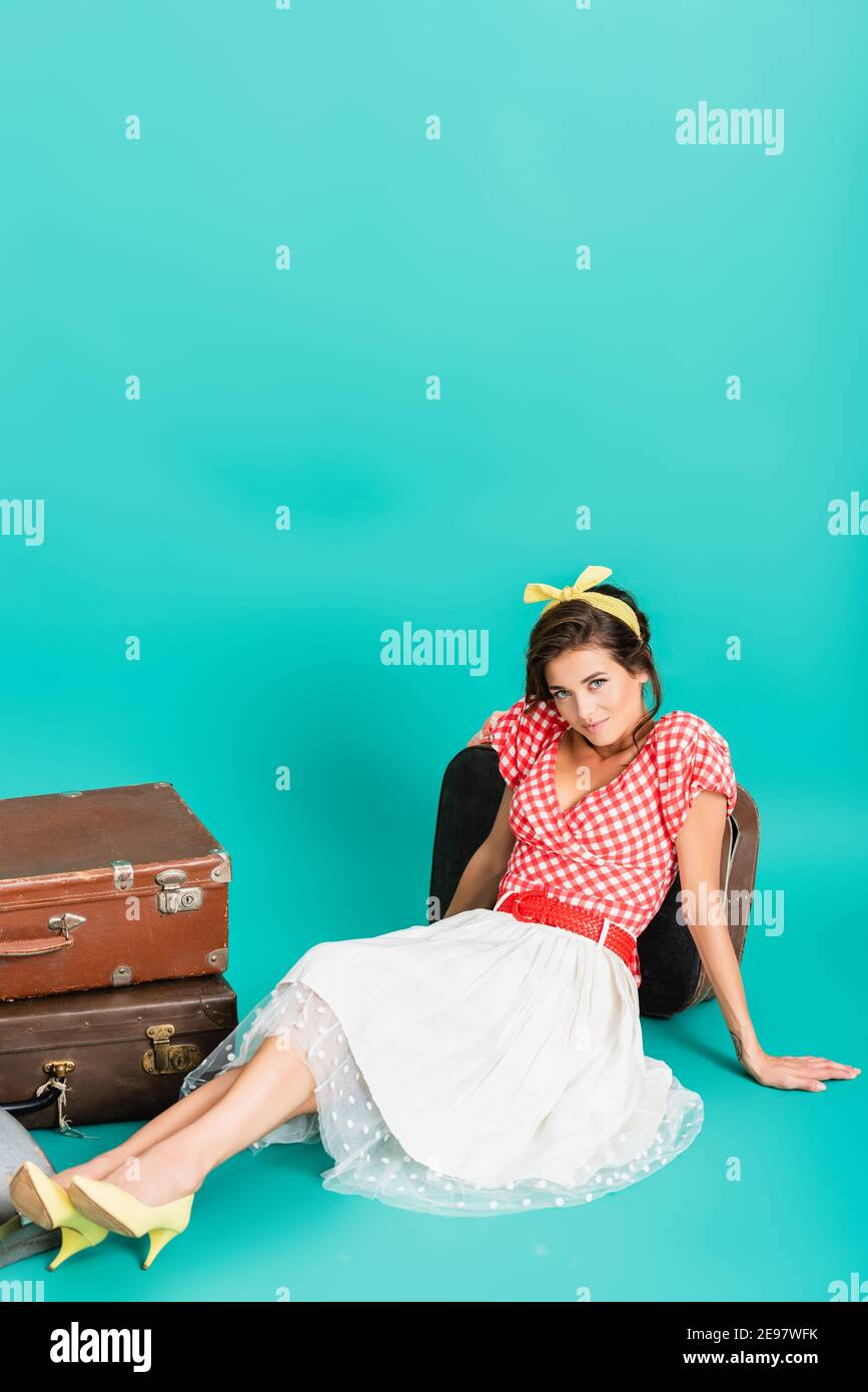 elegante pin up mujer sonriendo en la cámara mientras se sienta cerca  maletas vintage en color turquesa Fotografía de stock - Alamy