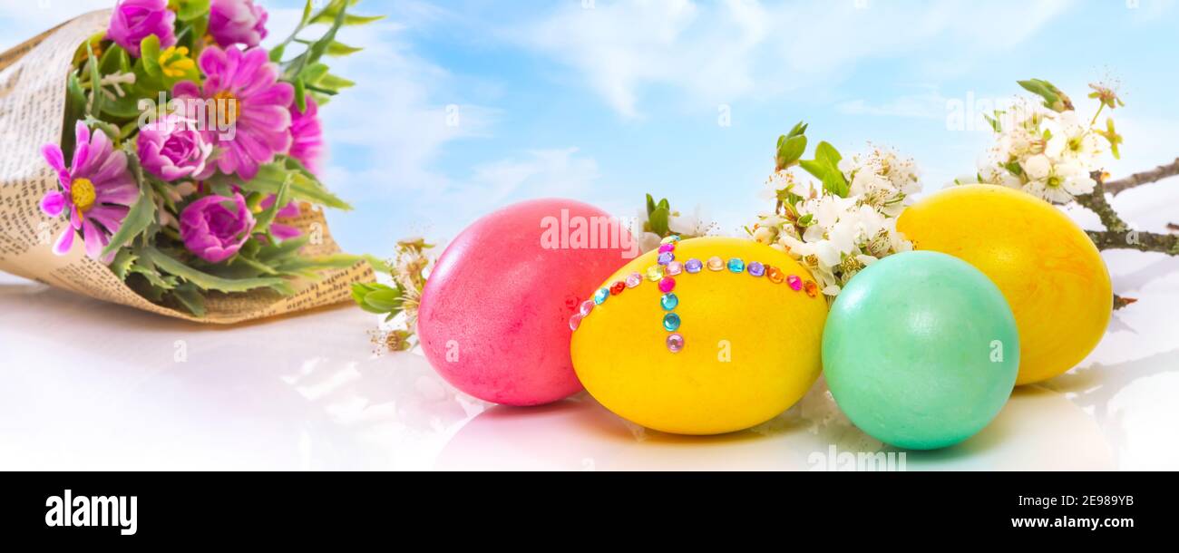 Huevos de Pascua de colores sobre el cielo azul nublado con ramo de flores, primer plano, banner de vacaciones Foto de stock