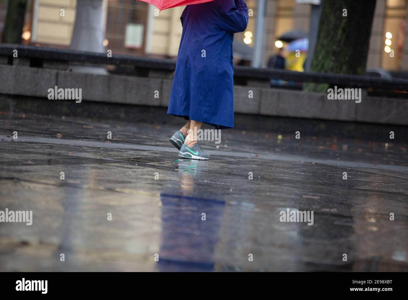 Lviv, Ucrania - 30 de septiembre de 2020: Mujer mayor con zapatillas Nike y  paraguas rojo caminando en la calle lluviosa Fotografía de stock - Alamy