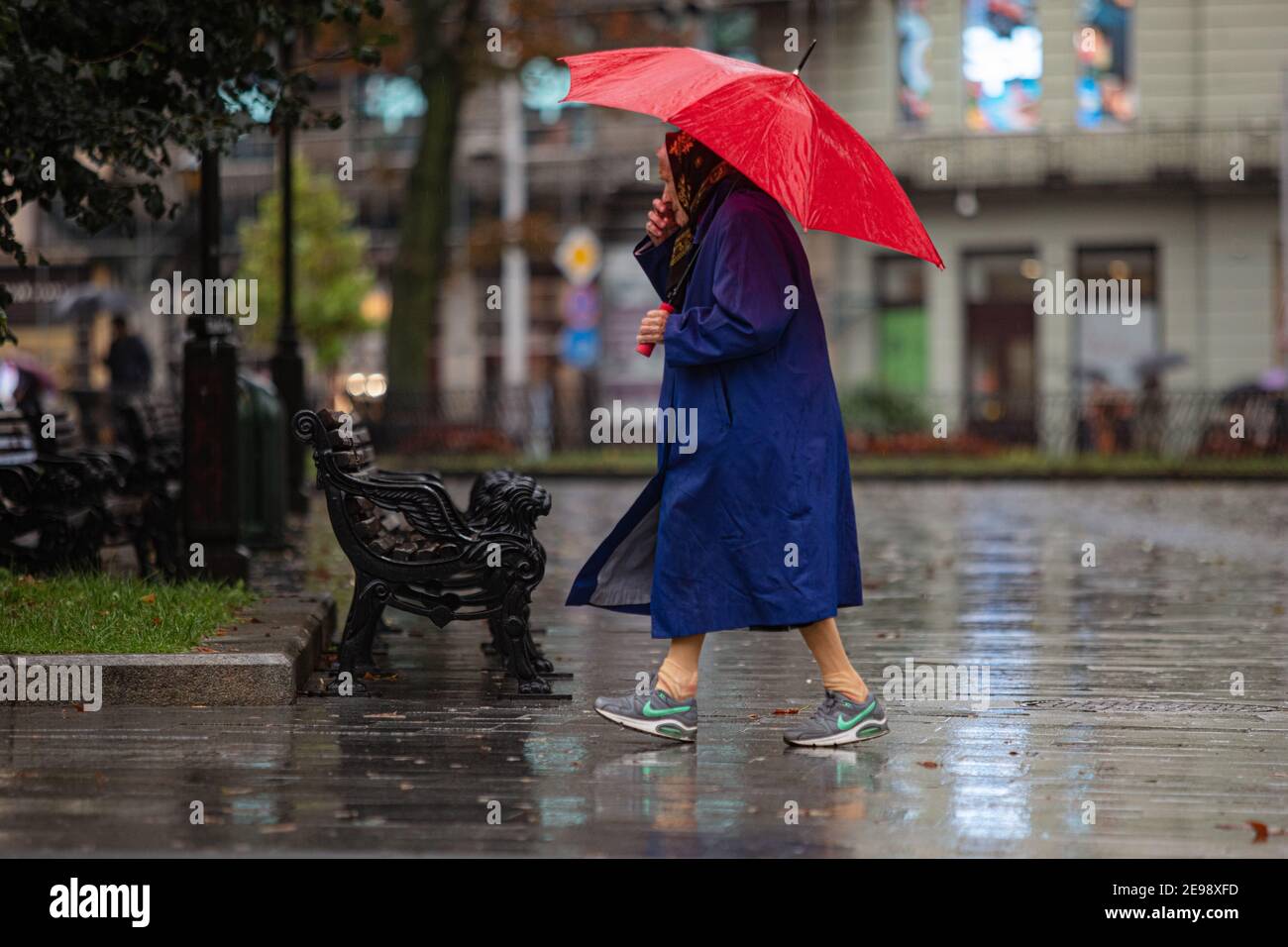 Lviv, Ucrania - 30 de septiembre de 2020: Mujer mayor con zapatillas Nike y  paraguas rojo caminando en la calle lluviosa Fotografía de stock - Alamy