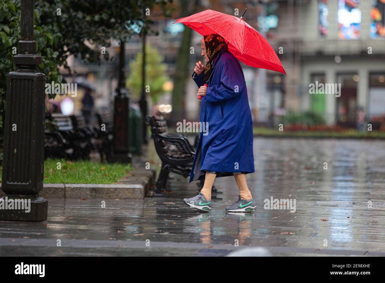 Lviv, Ucrania - 30 de septiembre de 2020: Mujer mayor con zapatillas Nike y  paraguas rojo caminando en la calle lluviosa Fotografía de stock - Alamy