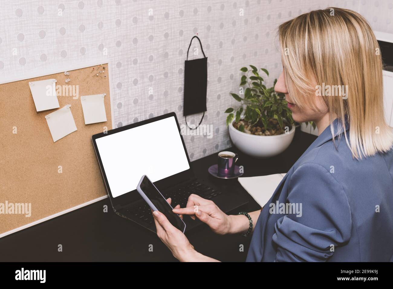 Concepto de asistencia sanitaria. Mujer rubia trabajando con computadora con pantalla blanca en blanco para copiar espacio y hablar con teléfono celular desde casa durante la cuarentena Foto de stock