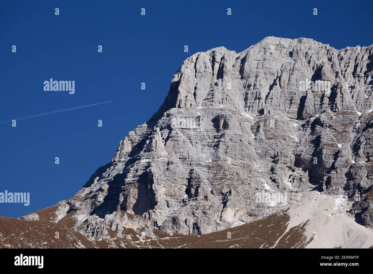 Empinadas laderas rocosas de la montaña Montaž en los Alpes Julianos con un avión volando sobre ella. Foto de stock
