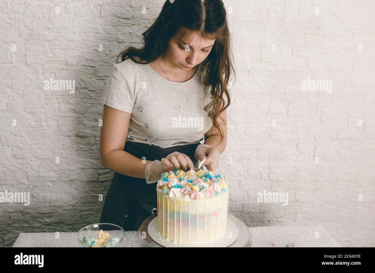Un chef de pastelería hace un pastel de boda con sus propias manos y pone decoraciones coloridas en los pasteles con crema. Preparación para la celebración Foto de stock