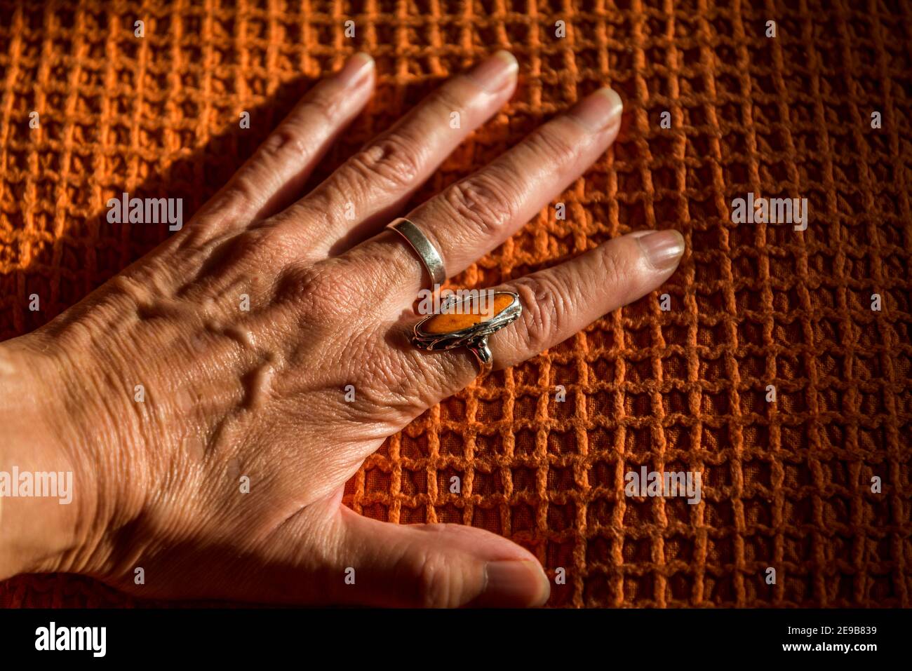 Mano femenina con un anillo naranja en una cubierta naranja Foto de stock