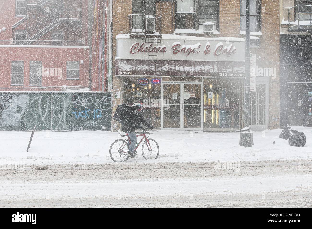 New York City , NY USA Entrega de bicicletas Persona en la nieve frente a Chelsea Bagel y Café en la calle 14th Foto de stock