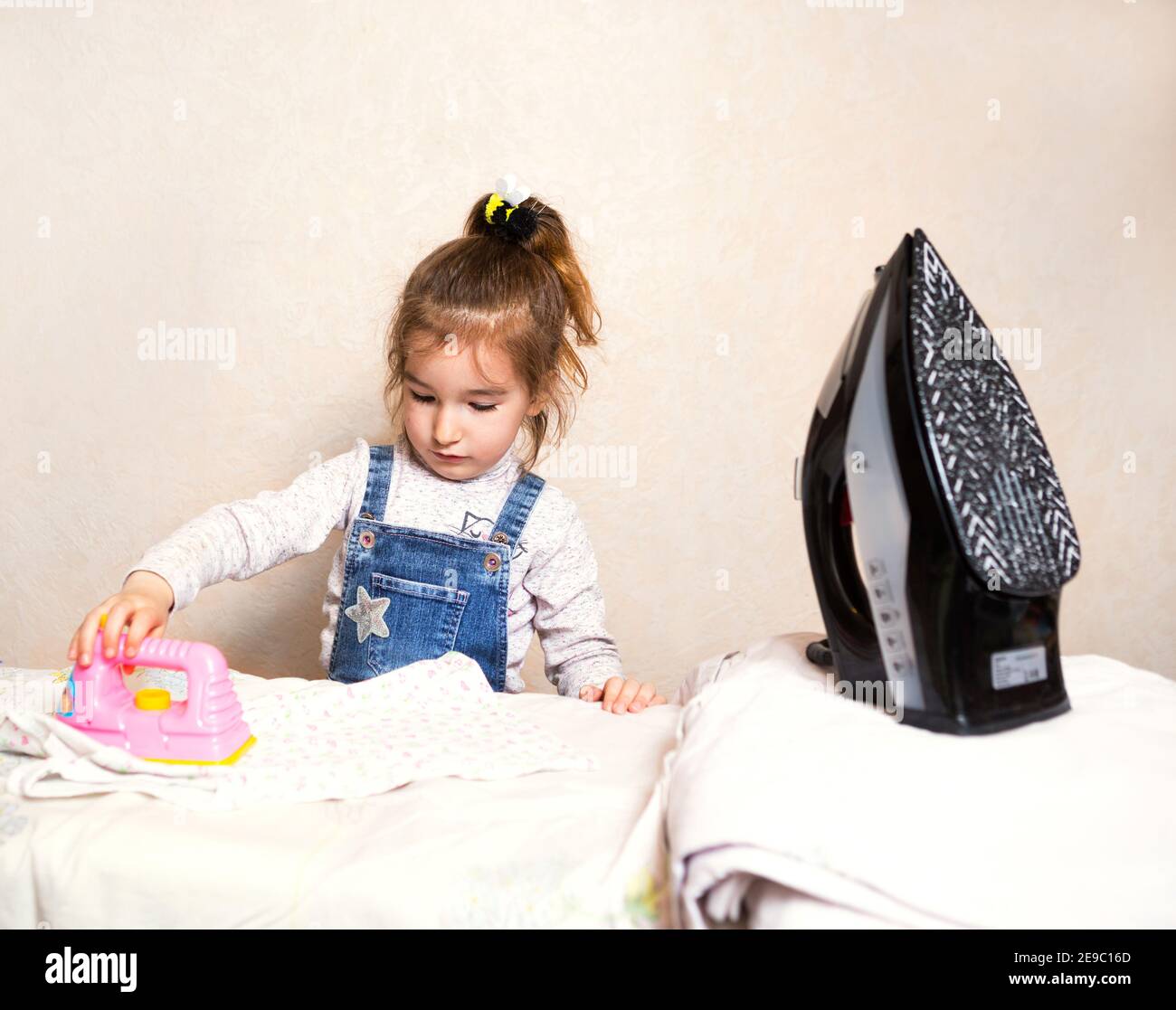 Una niña está planchando ropa con una plancha de juguete. Asistente de mamá, juegos para niños, tareas Fotografía de stock - Alamy