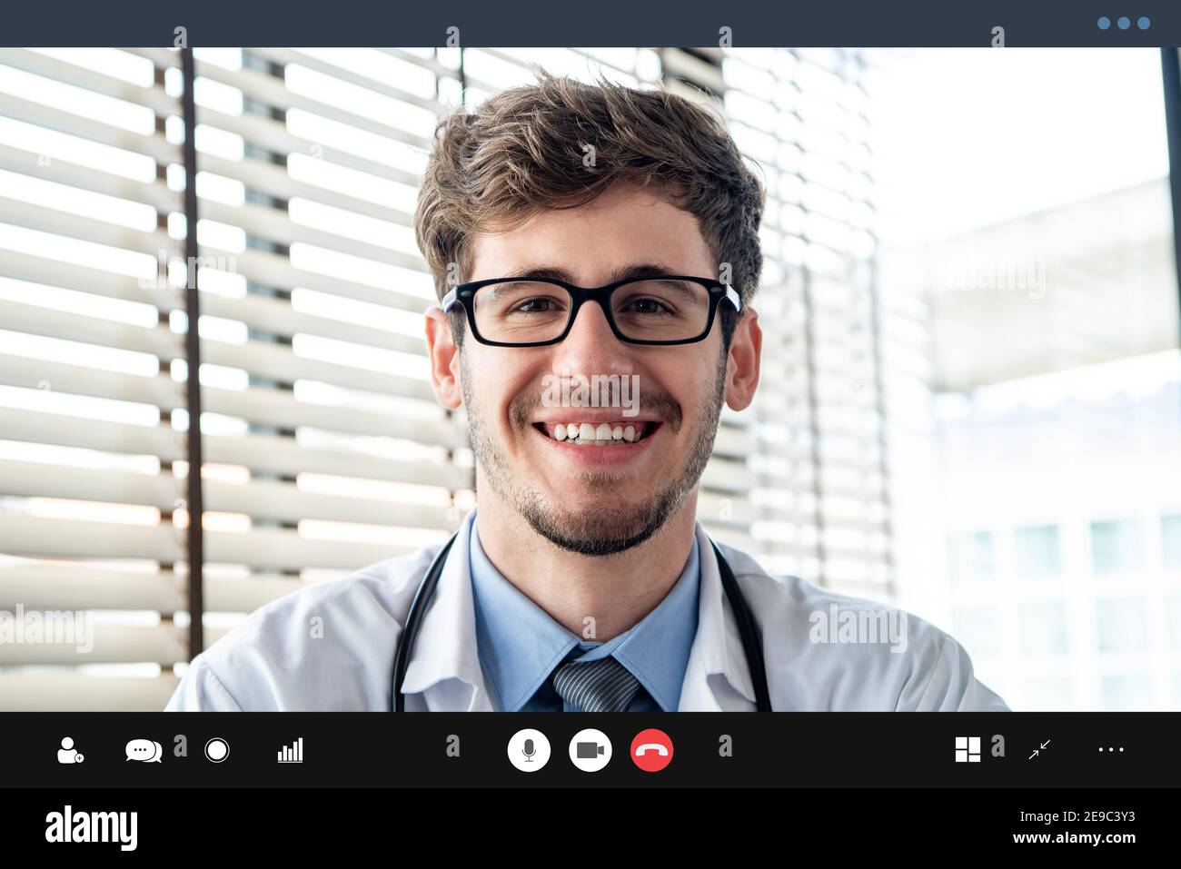 Un joven médico sonriendo a la cámara mientras hace una videollamada con el paciente en línea, hogar médico conceptos de servicio de consulta Foto de stock