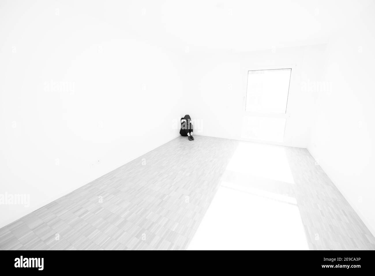 Mujer deprimida sentada en el piso en un rincón en una habitación vacía en casa en Suiza. Foto de stock