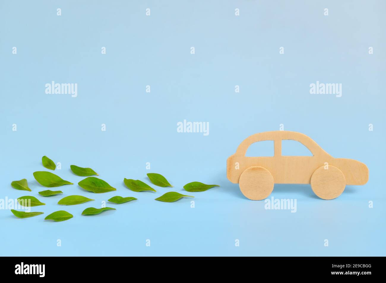 Modelo de coche de madera que emite hojas verdes frescas sobre fondo azul. Energía sostenible, limpia y verde y biocombustible y biodiesel para el transporte Foto de stock