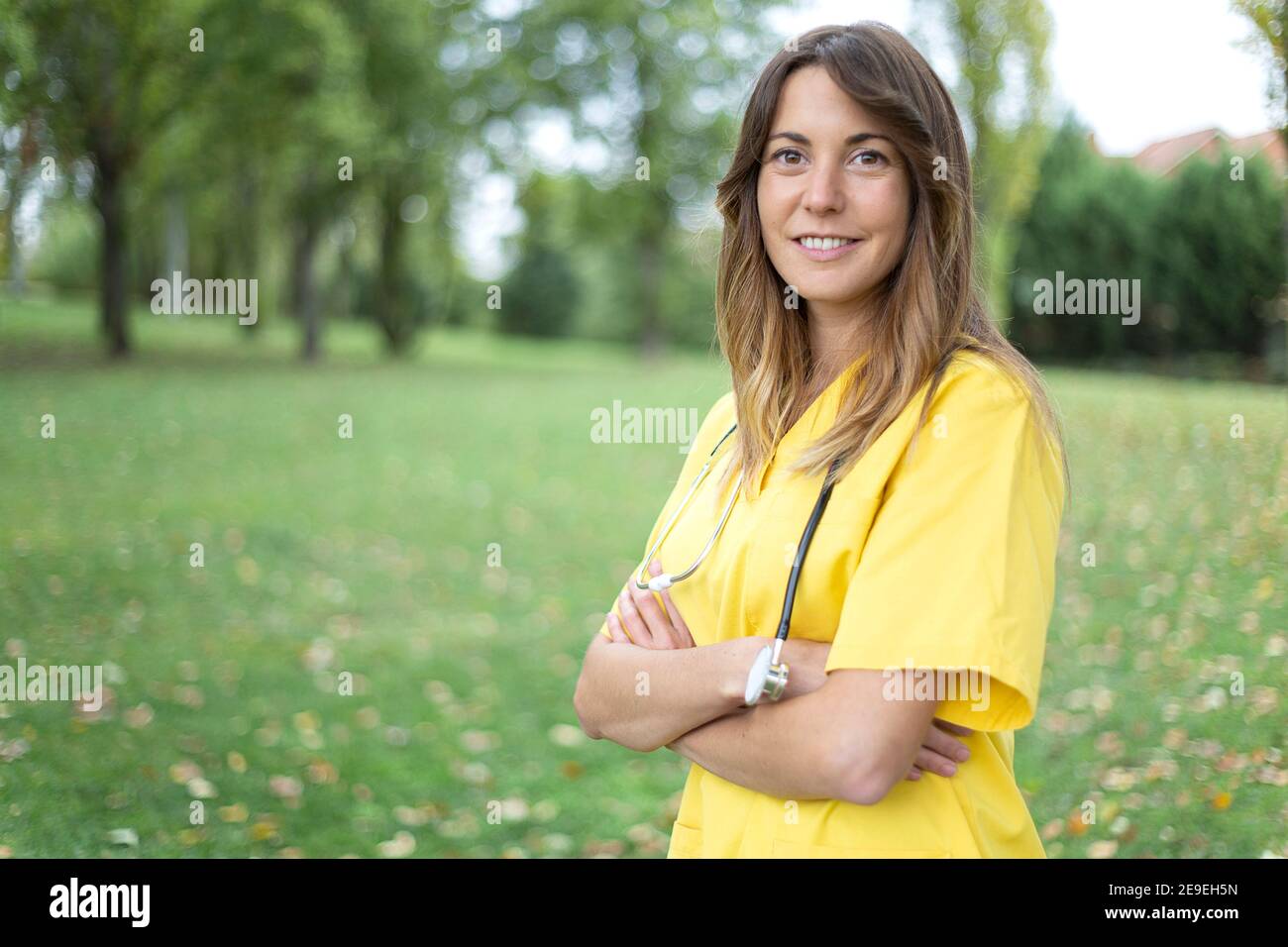 Retrato de la enfermera caucásica con sus brazos cruzados en postura segura. Ella está al aire libre. Espacio para texto. Foto de stock