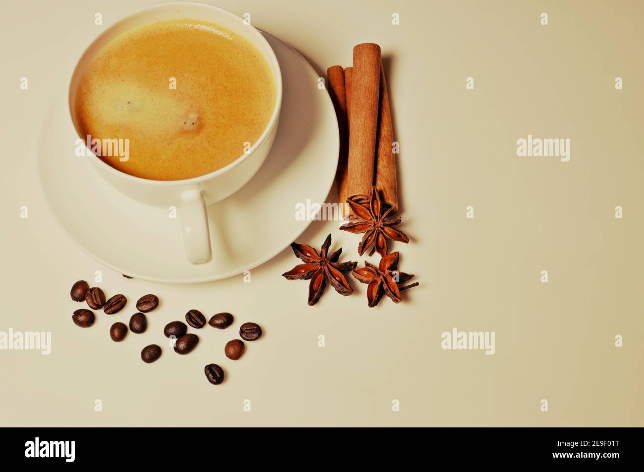 Taza de café caliente con canela, granos de café y decoración de estrellas de anís sobre fondo blanco de mesa. Filtro aplicado, tabla superior Foto de stock
