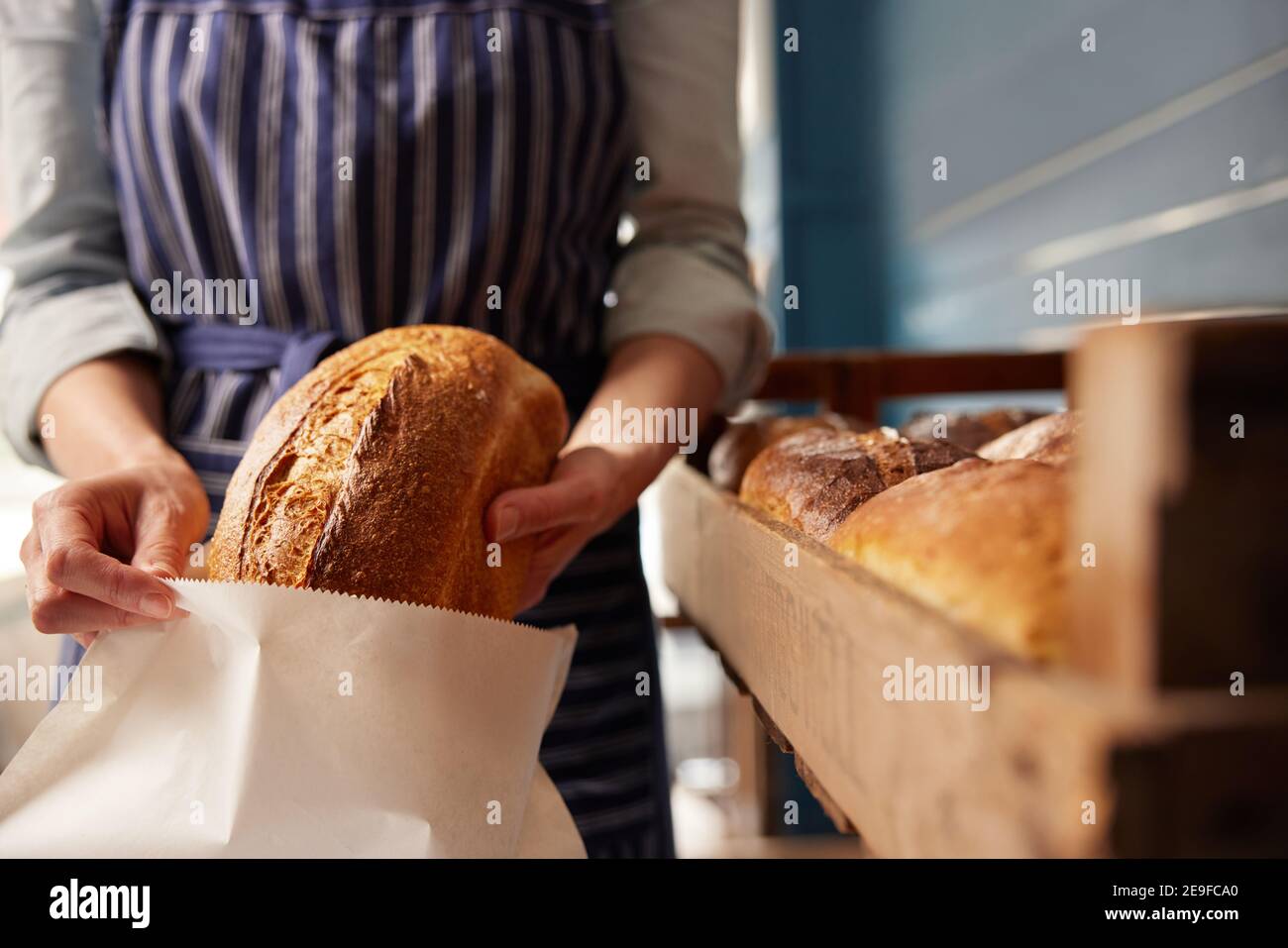 Asistente de ventas en panadería poniendo pan de masa orgánica recién horneado Haz un pan en una bolsa de papel sostenible Foto de stock