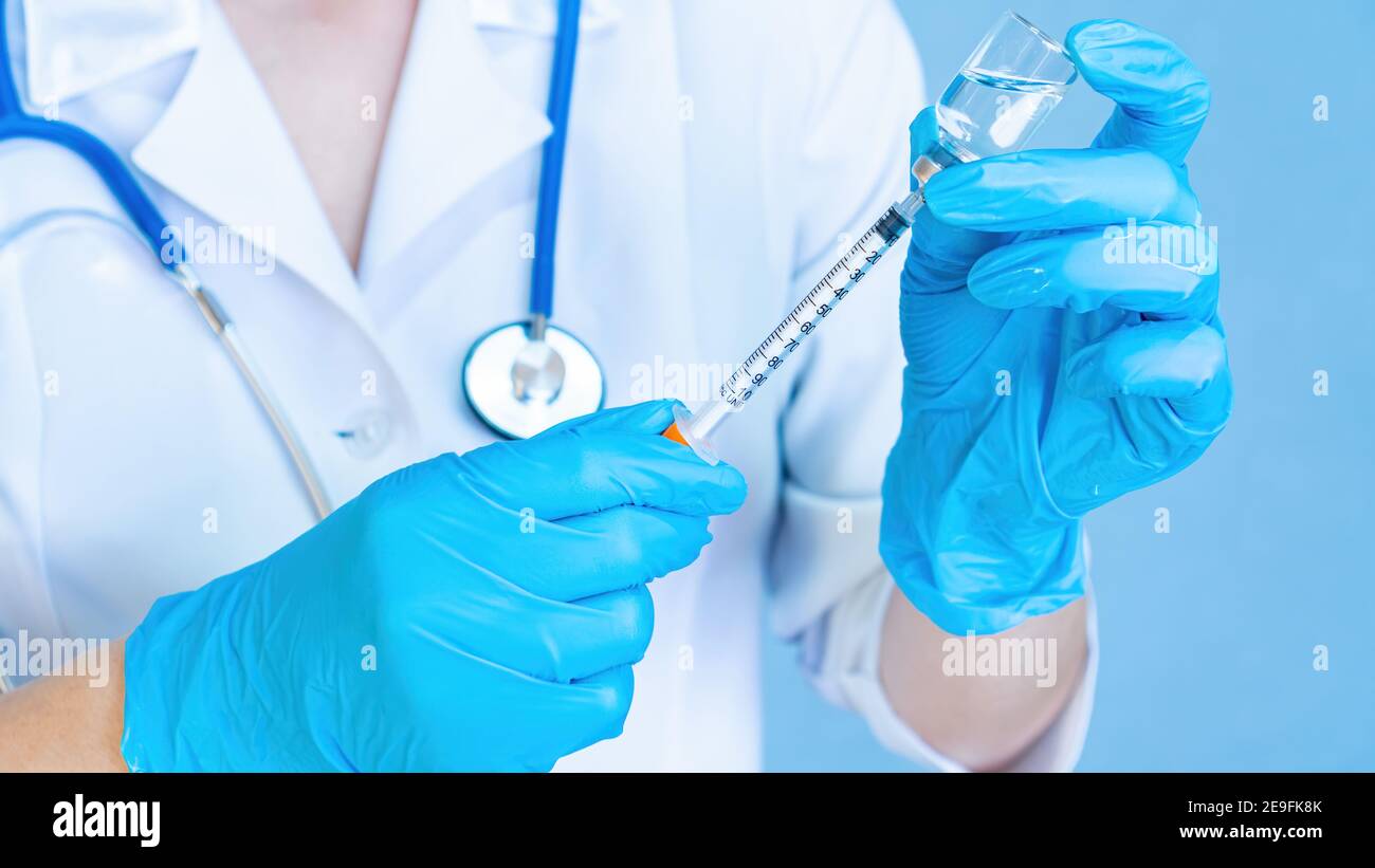 Un médico con un estetoscopio en guantes médicos está llenando una jeringa de un vial con medicamento o vacuna contra el coronavirus. Preparación para la insulina i. Foto de stock