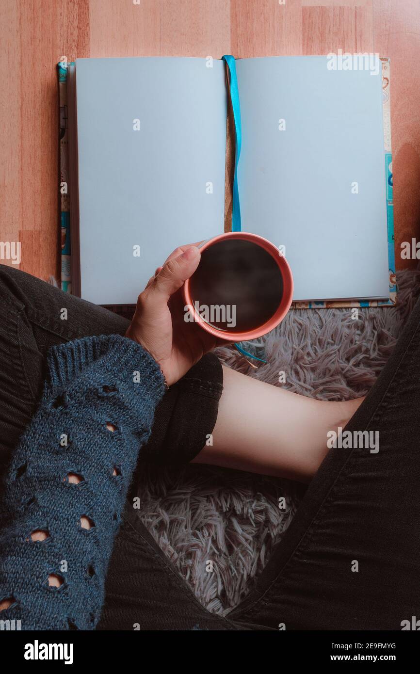 Primer plano de una mujer bebiendo una taza de café caliente, muy cómoda y leyendo un libro Foto de stock