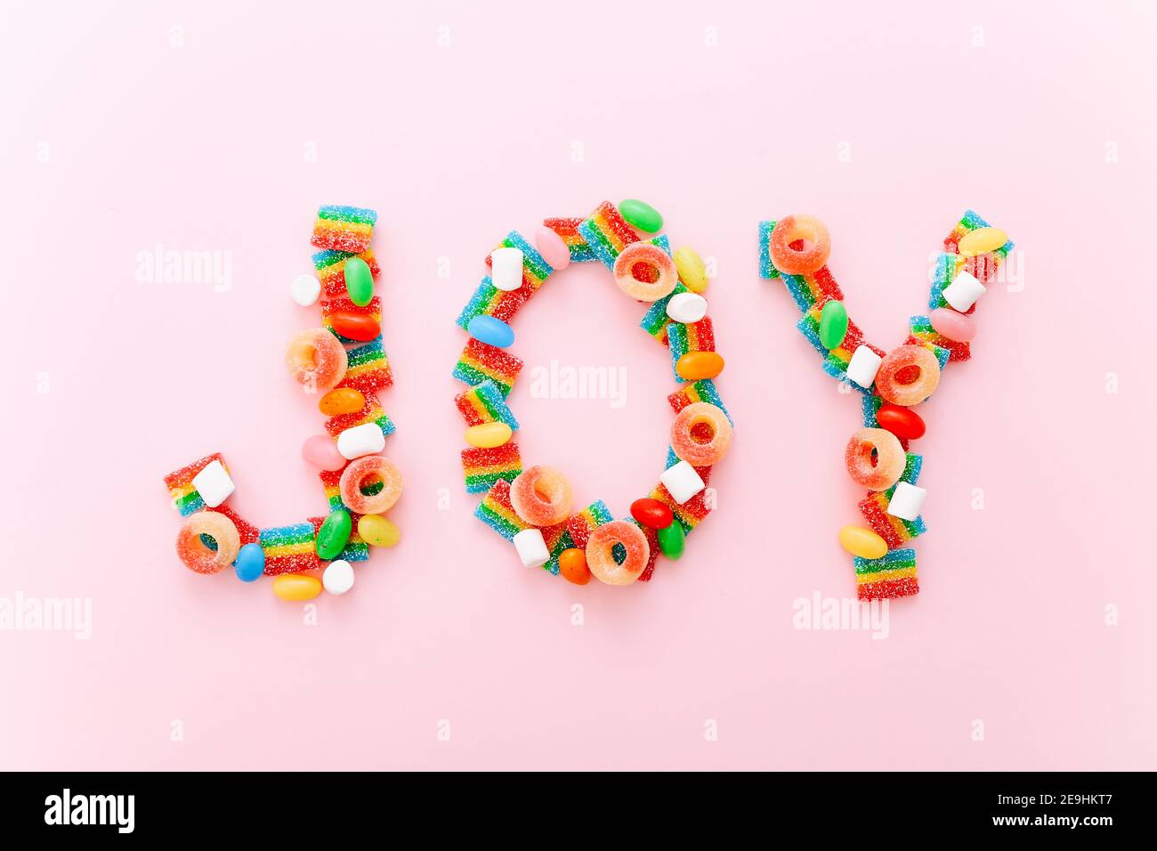 Palabra alegría hecha de caramelos de color sobre un fondo rosa Foto de stock