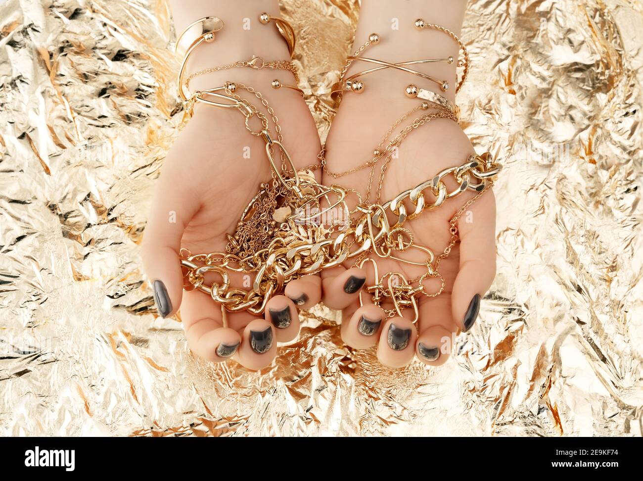 Manos femeninas con moderno diseño de uñas oscuras con pulseras doradas sobre fondo dorado. Concepto de lujo. Un telón de fondo festivo para tu diseño. Vista superior. Foto de stock