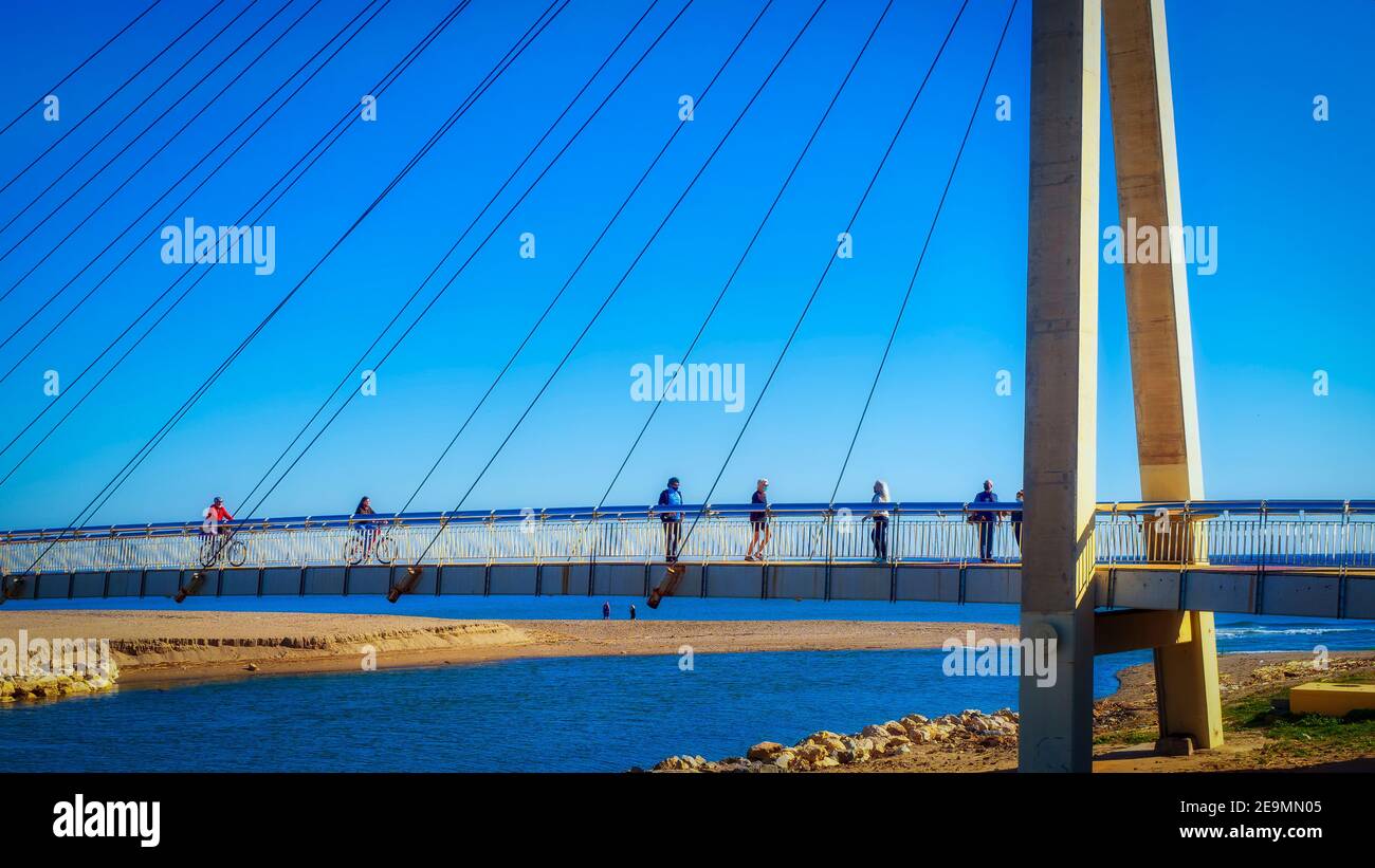 Fuengirola, Málaga, España. Enero de 2021. Varias personas cruzan el río Fuengirola por un puente colgante en un soleado día de invierno. Foto de stock