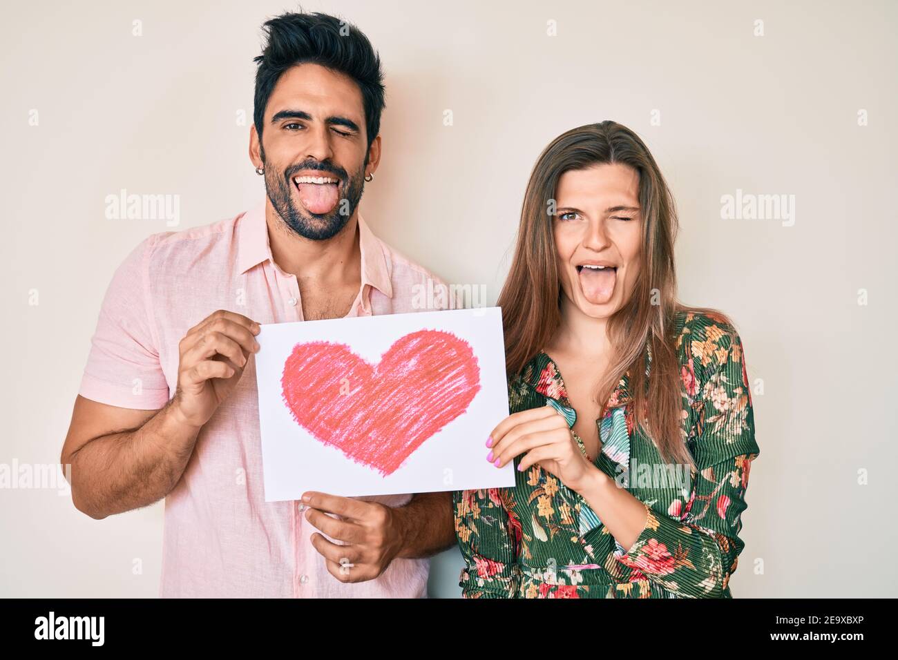 Hermosa pareja joven juntos sosteniendo el corazón sacar la lengua fuera  feliz con la expresión divertida Fotografía de stock - Alamy