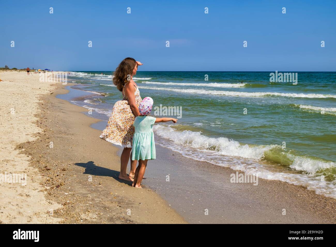 Hija muestra a mamá algo muy lejos en el mar Foto de stock