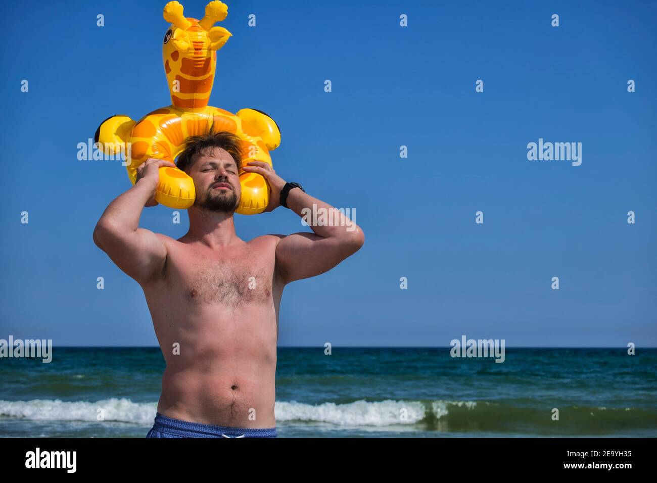 El hombre en la orilla puso una jirafa inflable en su la cabeza y cubrió sus ojos de la luz del sol brillante Foto de stock