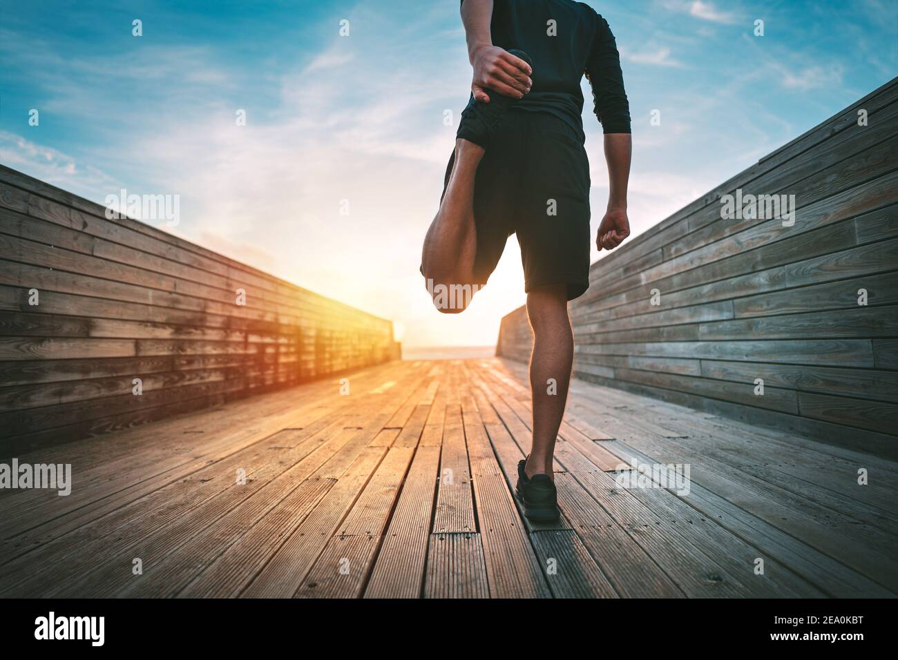 Hombre calentando y estirando las piernas antes de correr al aire libre al atardecer o amanecer Foto de stock