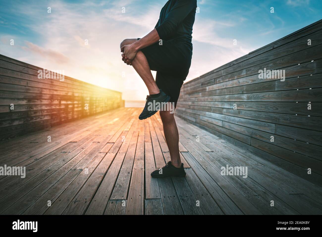 Hombre calentándose y estirando las piernas antes de entrenar al aire libre en puesta de sol o salida del sol Foto de stock