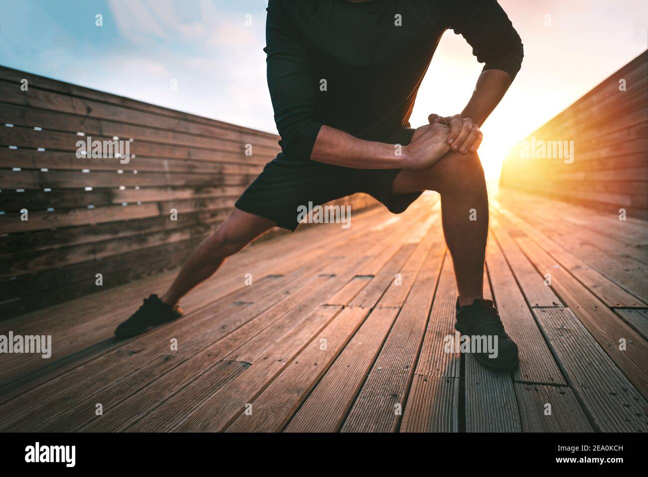 Hombre estirando los músculos aductores de la pierna y calentándose para entrenar al aire libre Foto de stock