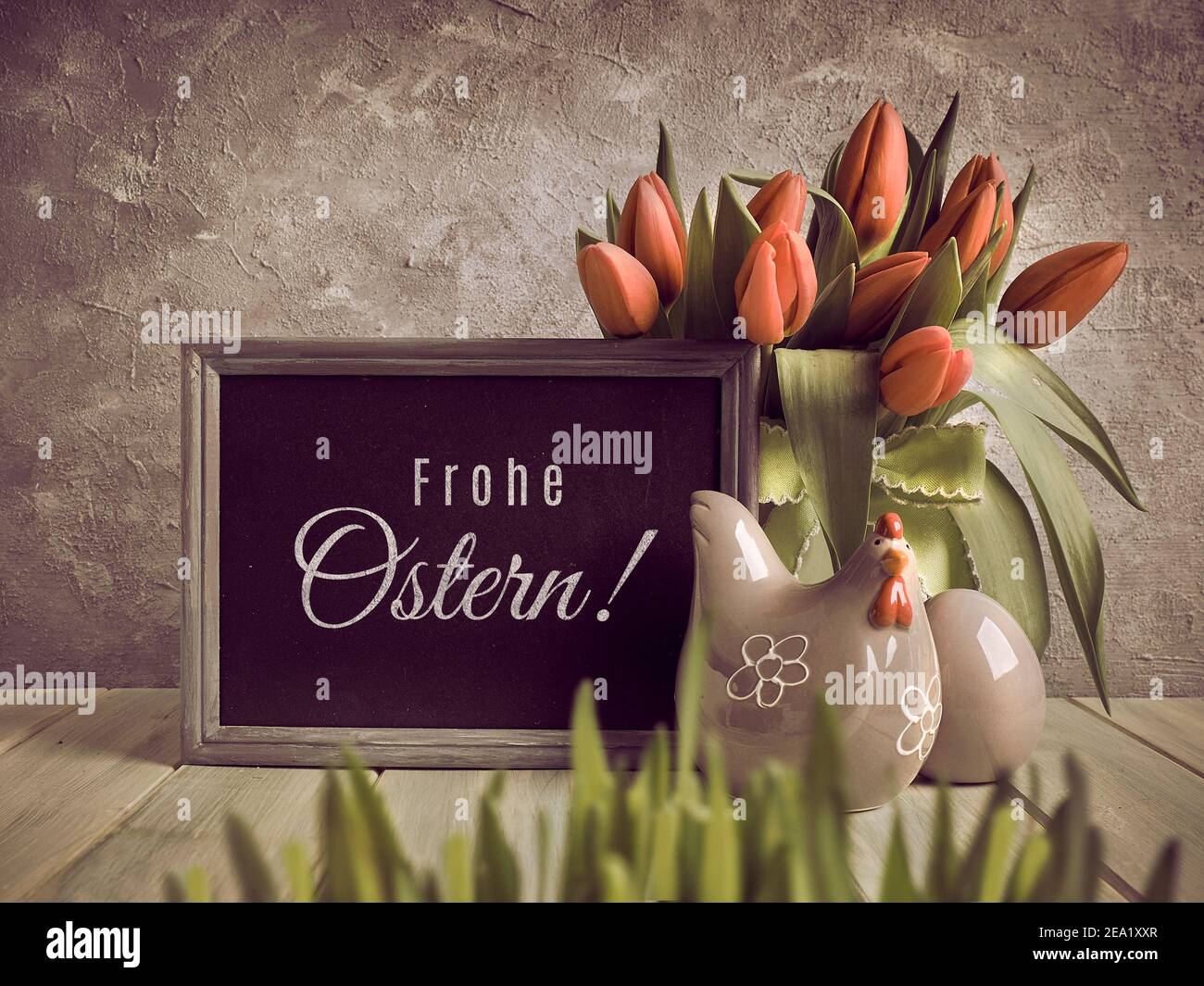 Frohe Ostern en alemán significa Semana Santa Feliz en inglés. Celebración de cumpleaños de Pascua o primavera. Manojo de tulipanes y gallina de cerámica con huevo sobre madera Foto de stock