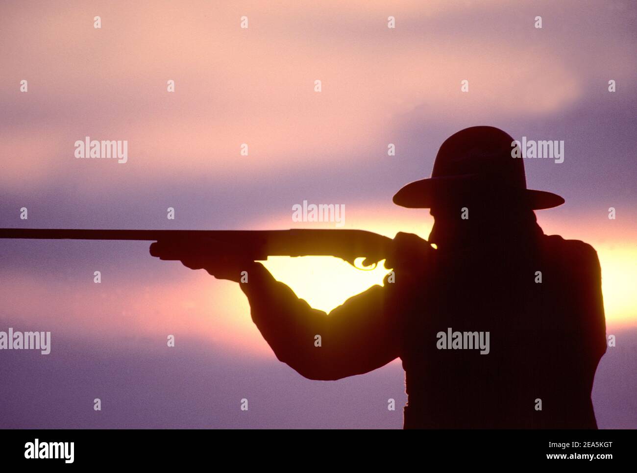 Silueta de cazador disparando escopeta al atardecer Foto de stock