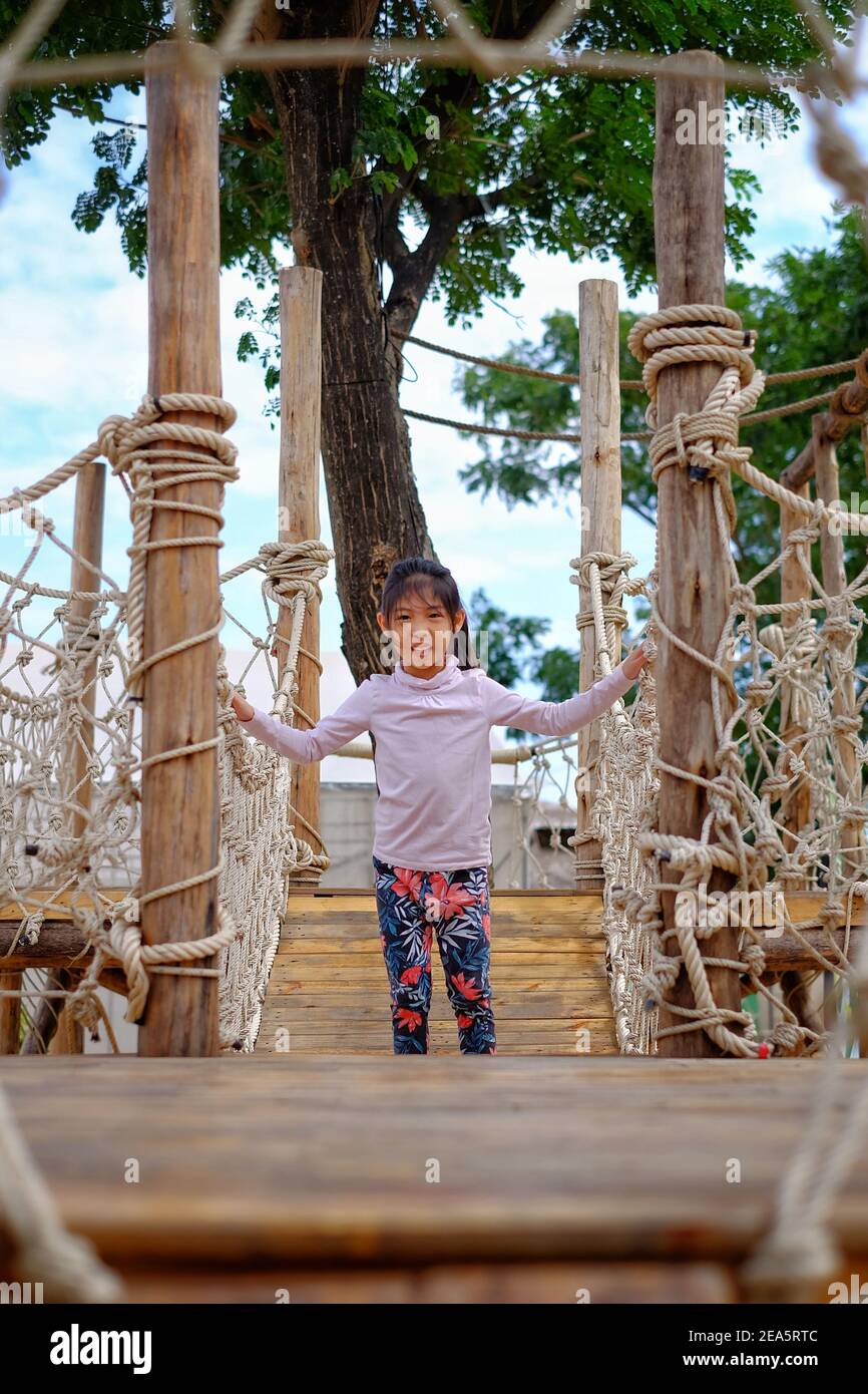 Una linda chica asiática jugando en un campo de obstáculos hecho de cuerdas y madera en un parque público. Foto de stock