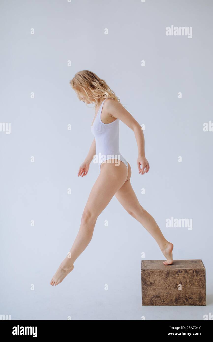 Gimnasta femenina en un leotardo blanco que baja de un bloque de madera Foto de stock