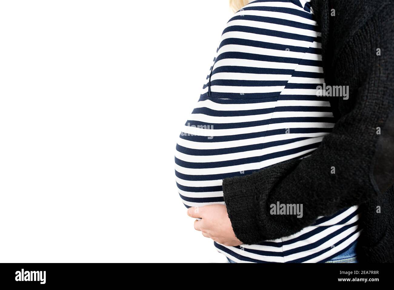 vista lateral de primer plano del baby bump de nueve meses de embarazo mujer con top de rayas y cárdigan de lana sobre fondo blanco Foto de stock