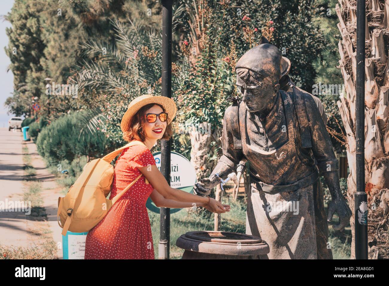 04 de septiembre de 2020, Turquía, Antalya: Mujer feliz se lava las manos en la calle en una fuente de primavera en forma de escultura de un portaagua. Foto de stock