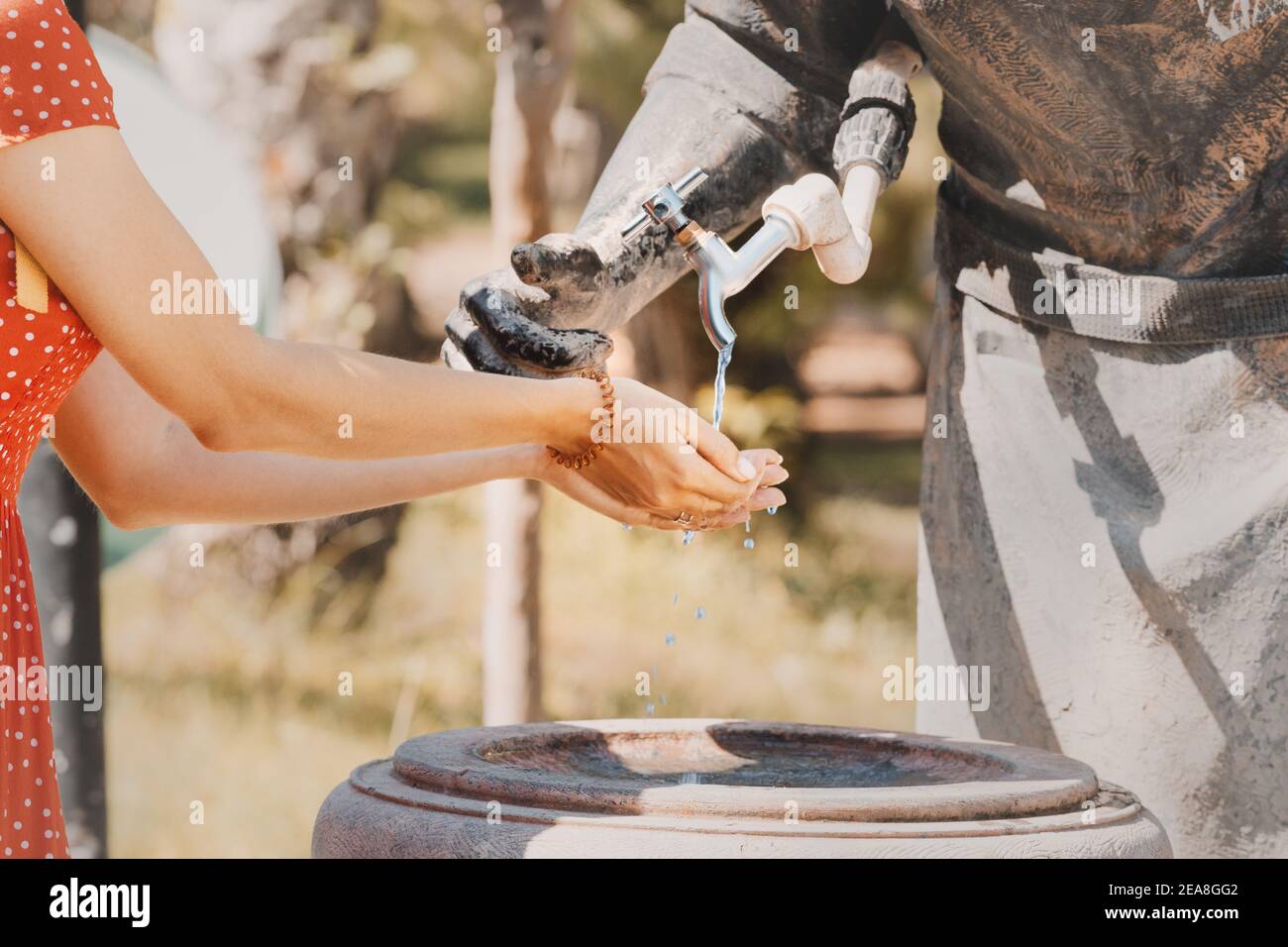 Mujer feliz lava sus manos en la calle en una fuente de primavera en la forma de una escultura de un portador de agua. Foto de stock