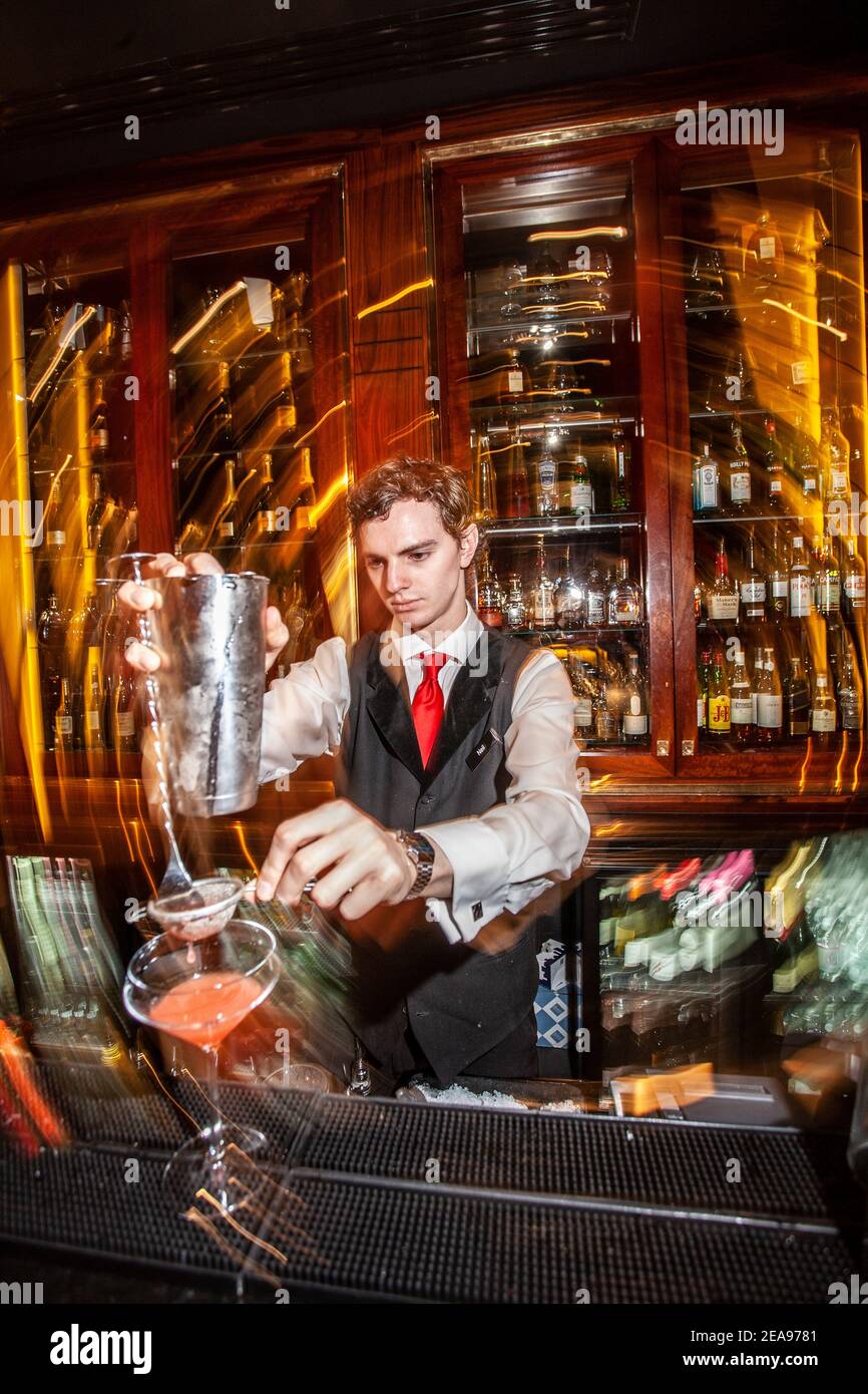 Un coctelero que trabaja detrás de un bar ocupado del hotel con un coctelero prepara una bebida. Foto de stock
