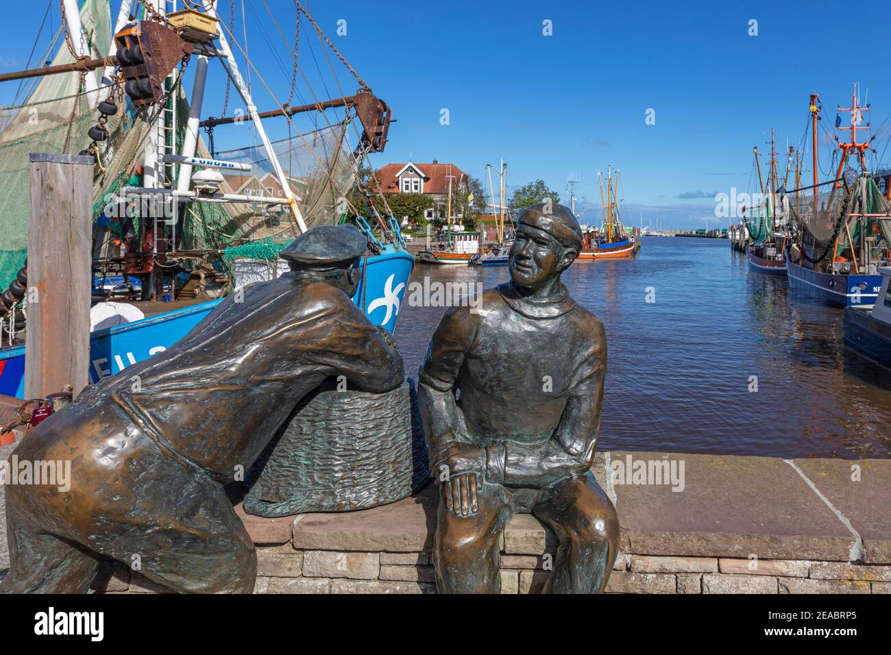 Pescador monumento antiguos y jóvenes pescadores, cortadores de camarones, en el puerto de Neuharlingersiel, Frisia Oriental, Baja Sajonia, Foto de stock