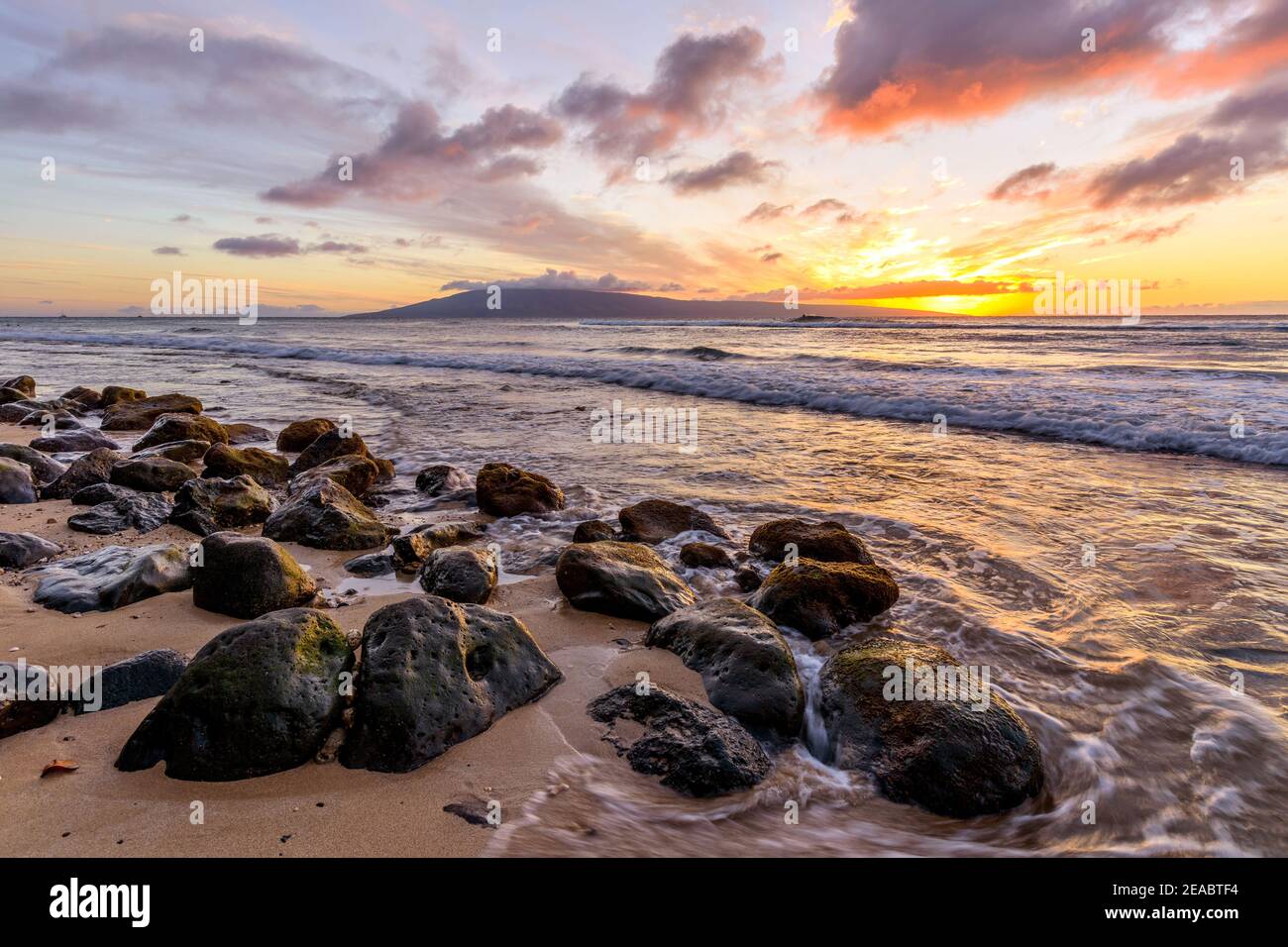 Puesta de sol tropical - una puesta de sol colorida en una playa rocosa de la costa noroeste de la isla de Maui, con la isla Lanai en el horizonte. Hawaii, EE.UU. Foto de stock