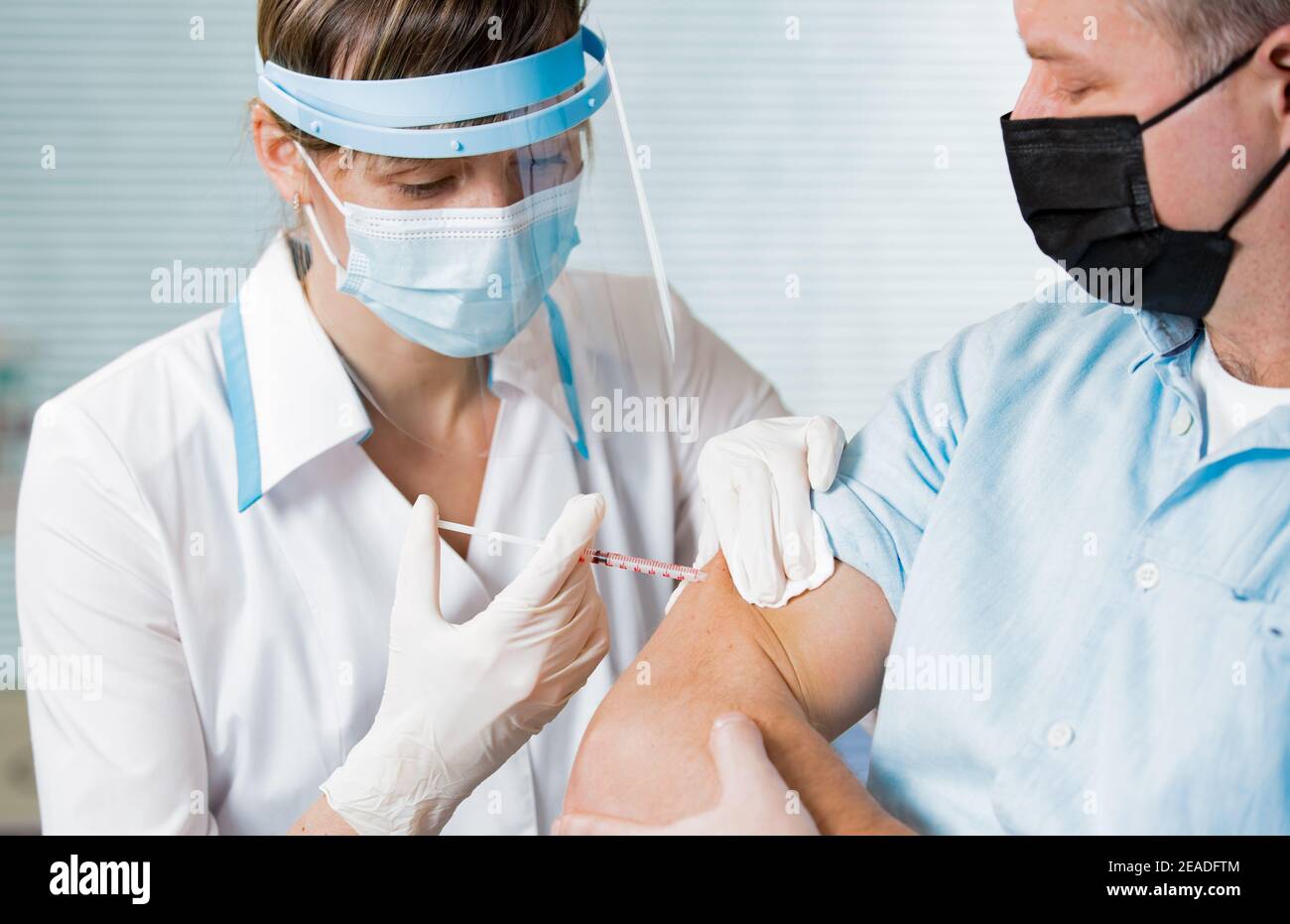 Médico femenino con máscara quirúrgica y en guantes que dan la inyección de la vacuna al hombre en el hospital. Vacunación durante la pandemia de COVID-19 Foto de stock