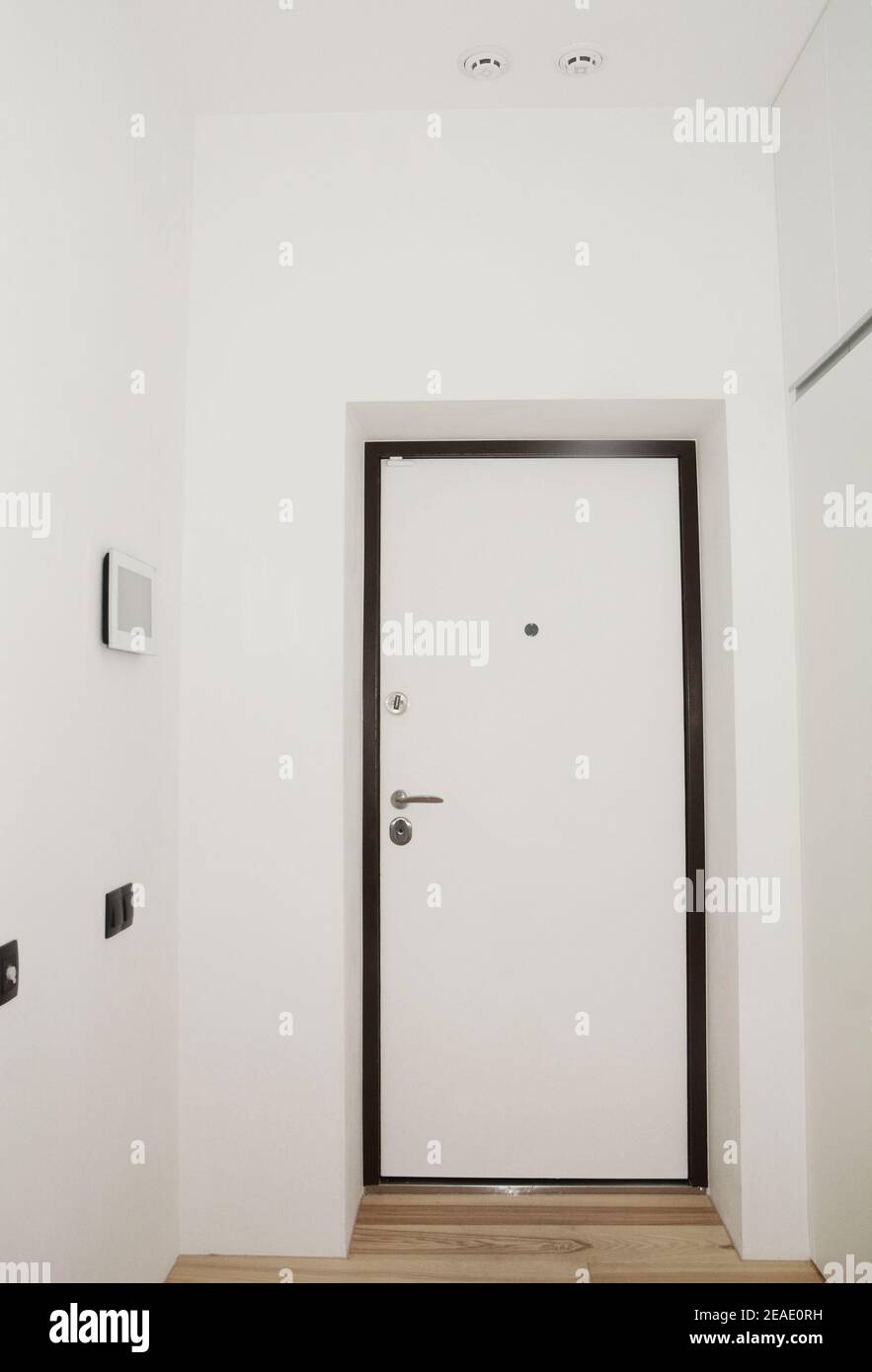 Vestíbulo de entrada blanco, entrada en un apartamento renovado con puerta blindada blanca y negra, un peepole, tirador de puerta y cerradura de puerta, detector de humo. Foto de stock