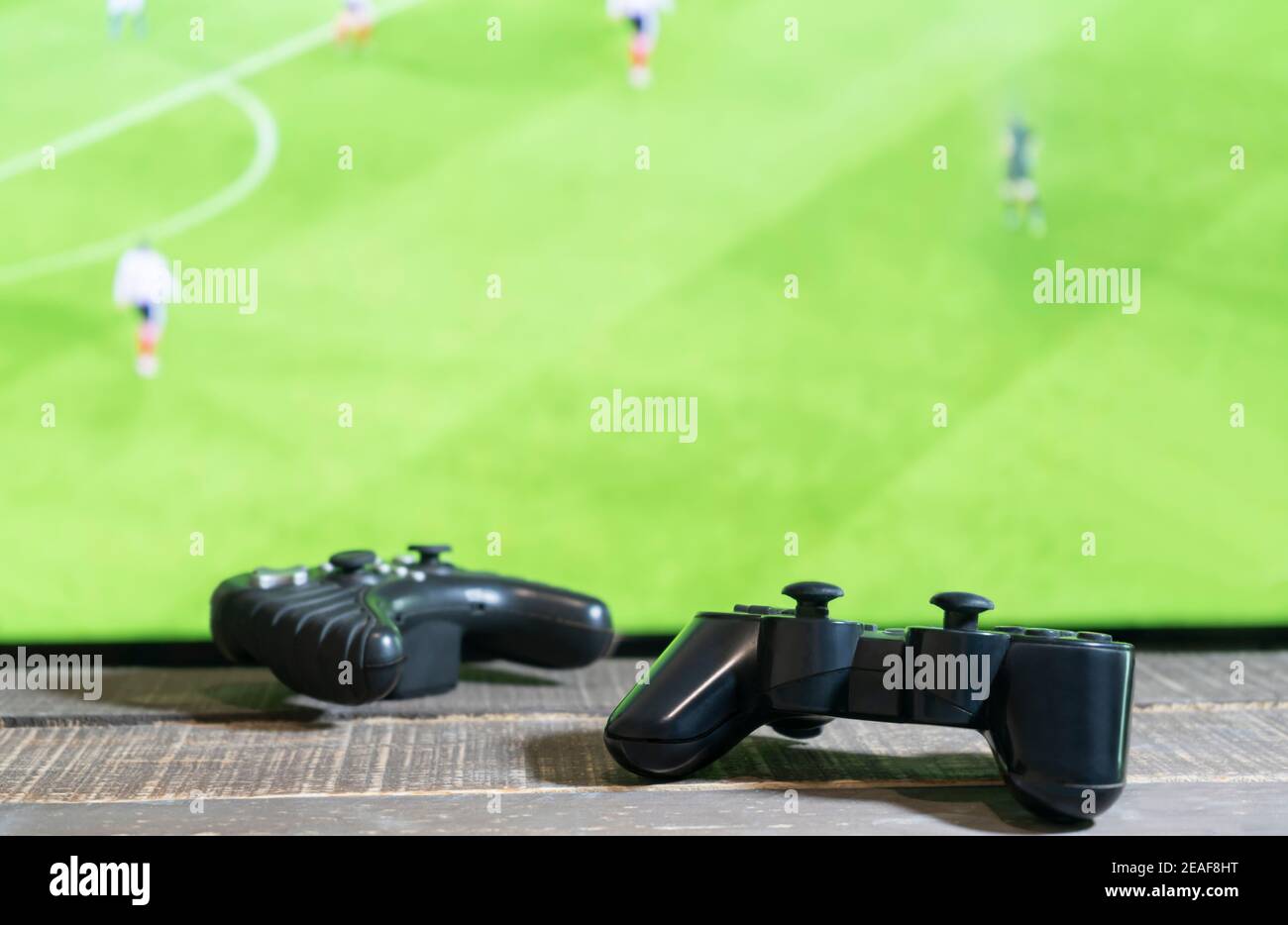Vista de cerca de dos mandos de consola de video de la almohadilla del juego con partido de fútbol, televisión de pantalla verde en el fondo.concepto del juego. Foto de stock