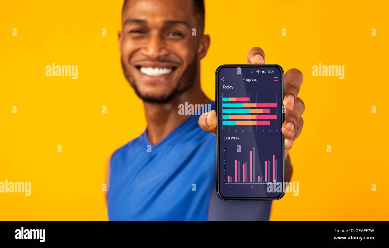 Hombre negro alegre que demuestra la aplicación en la pantalla del smartphone con el deporte progreso de la actividad Foto de stock