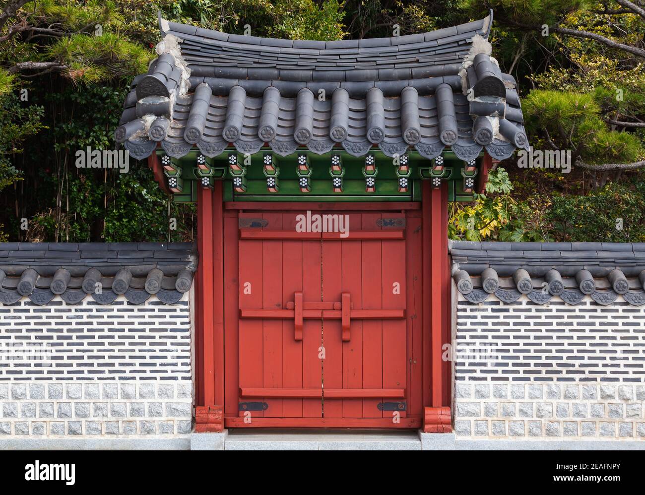 Puerta de madera roja bajo techo de baldosas en pared de piedra. Arquitectura oriental tradicional. Busan, Corea del Sur Foto de stock