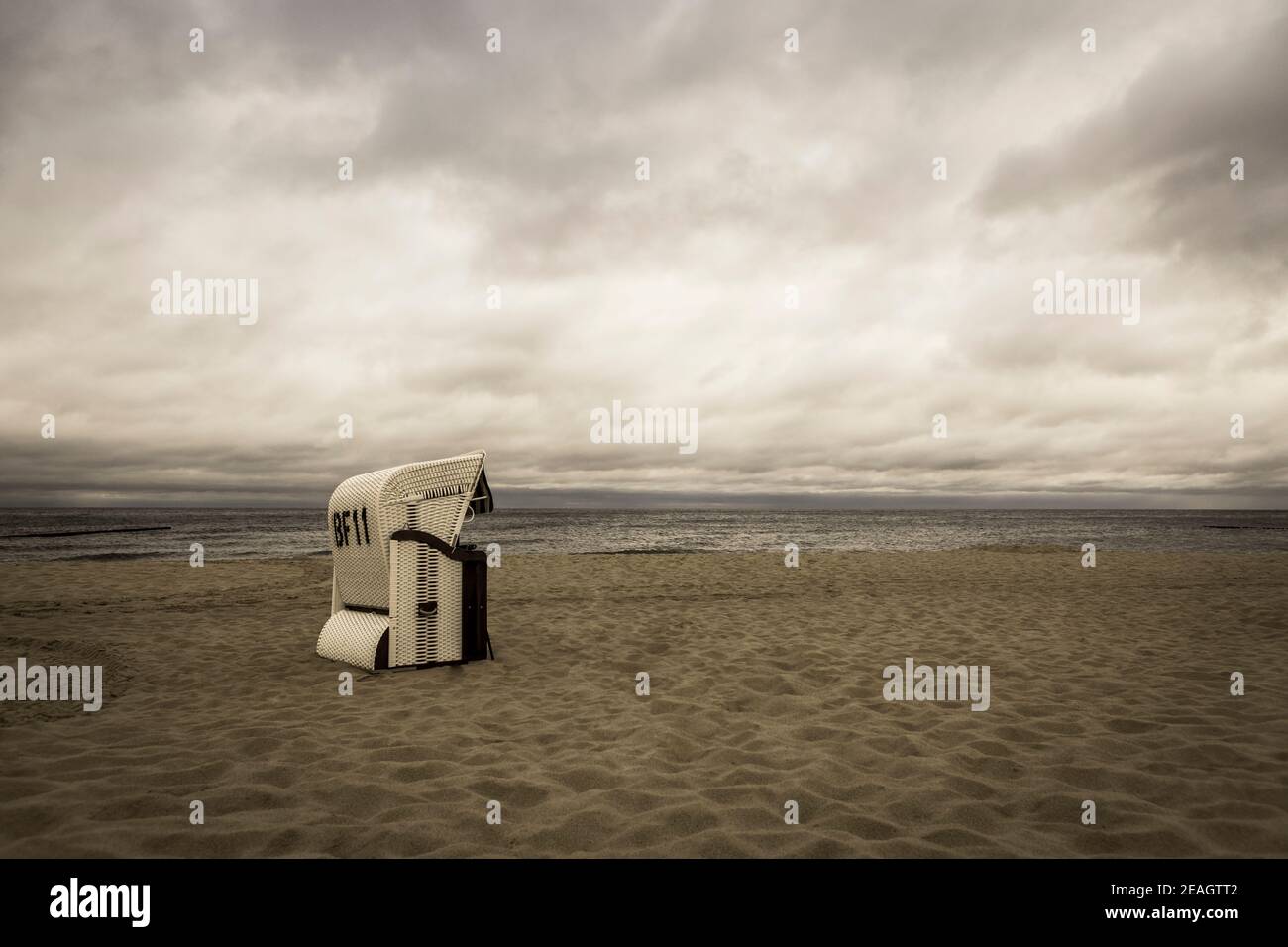 Nostalgia de las vacaciones y recuerdos lejanos concepto tiro de una playa escena con una silla de playa de mimbre y un cielo espectacular sepia Foto de stock