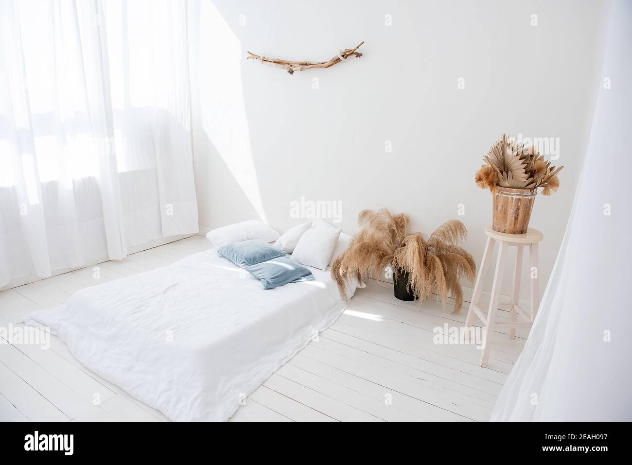 Loft blanco minimalista en estilo interior escandinavo. Hay una cama en el suelo de madera, los tulipanes ventilados y claros en las ventanas, hay pampas hierba en jarrones Foto de stock