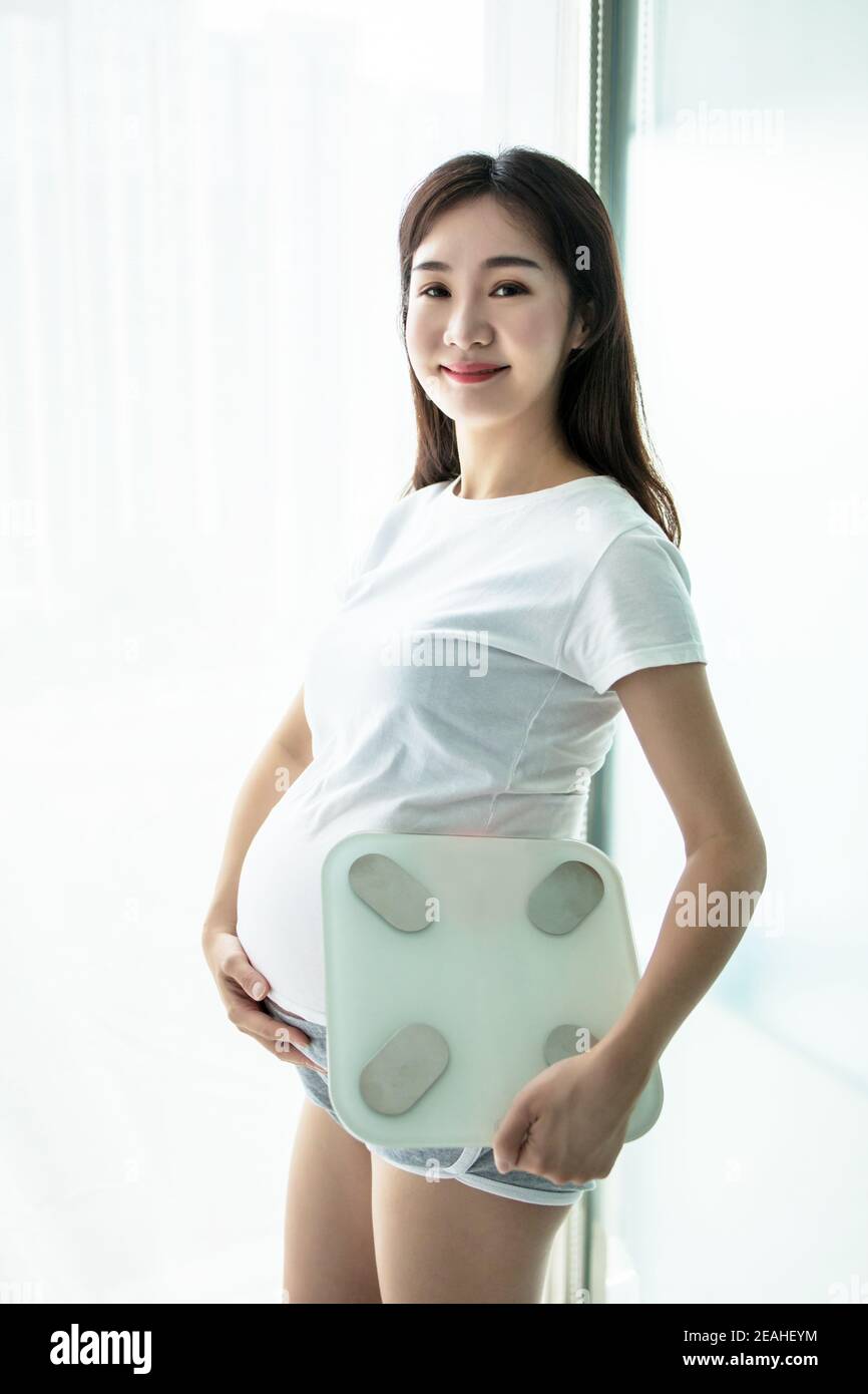 Mujer embarazada sosteniendo escamas y pesando manteniendo una mano en el  vientre. El concepto de pérdida de peso y control durante el embarazo  Fotografía de stock - Alamy