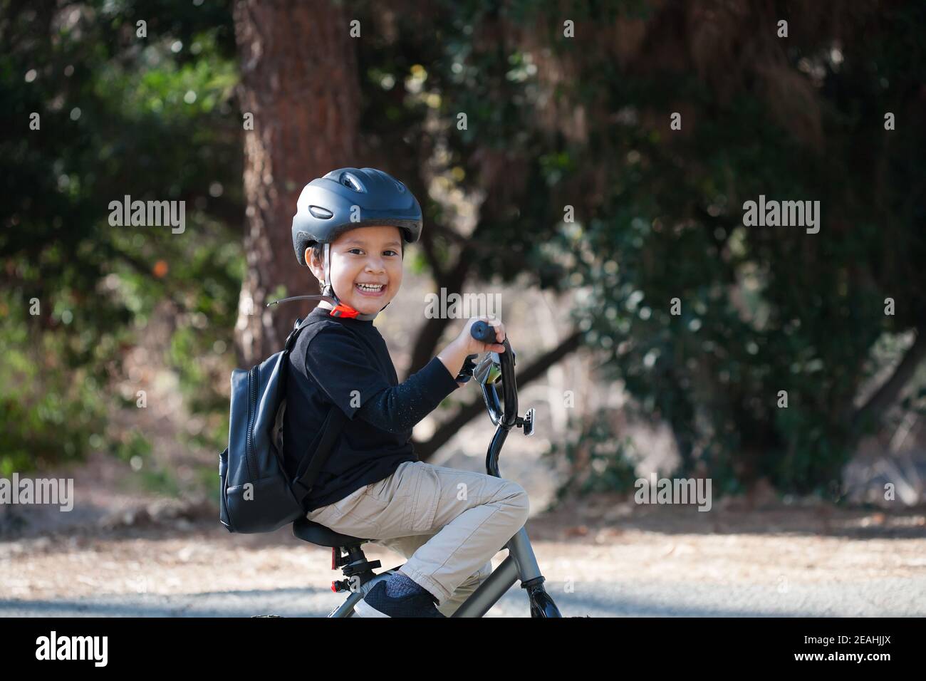 Niño en edad de kindergarten con una gran sonrisa mientras monta en bicicleta, usando una mochila y un casco para la protección. Foto de stock