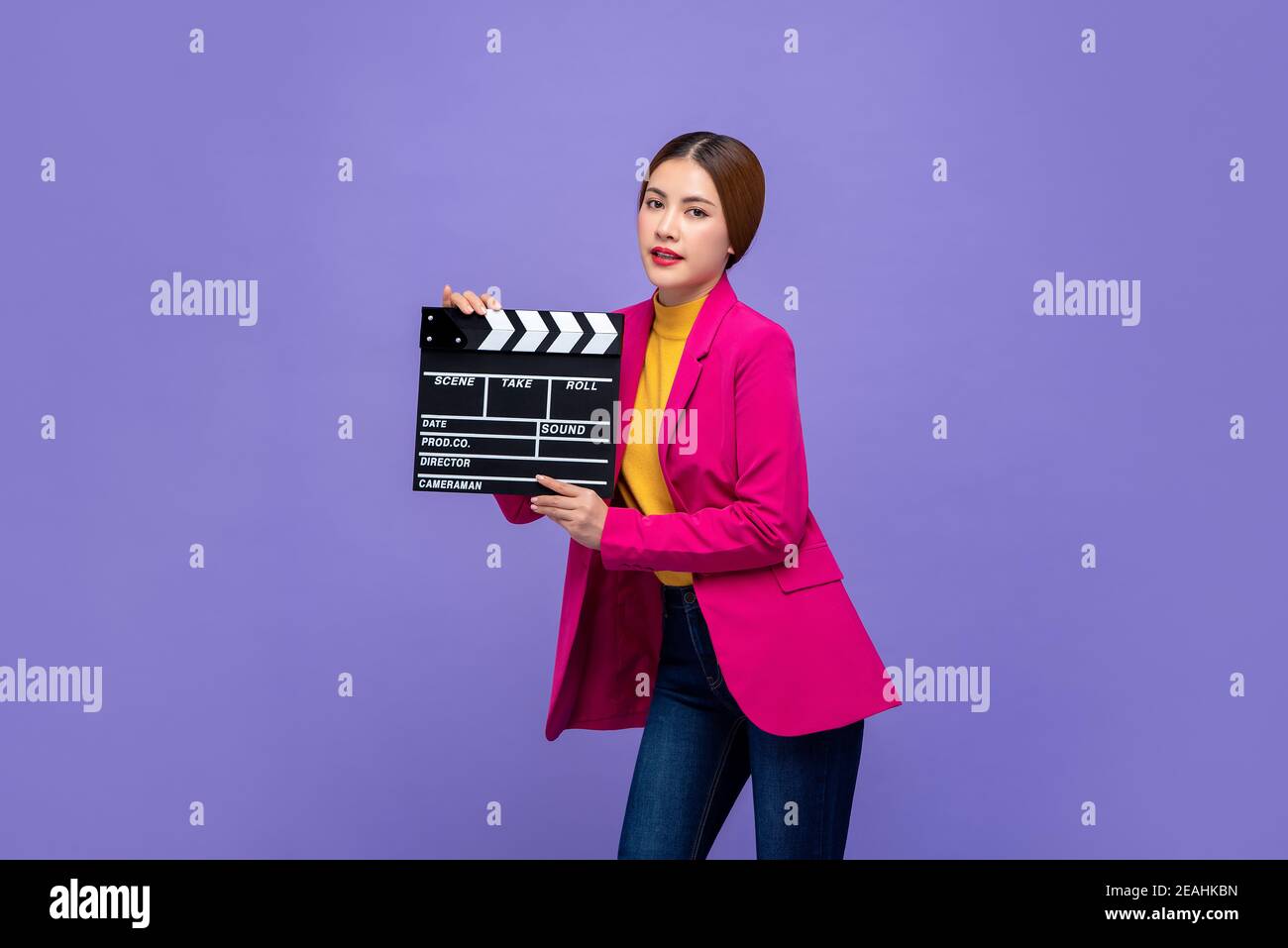 Joven hermosa mujer asiática modelo en ropa de colores sosteniendo la película clapperboard aislado sobre fondo púrpura Foto de stock