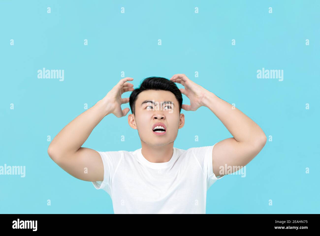 Enojado hombre asiático con las manos apretando la cabeza aislada fondo azul claro Foto de stock